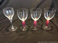 Four wine glasses displayed on a black background, one Schott Zwiesel and three Kosta Boda with red and blue striped stems