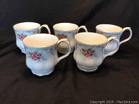Five Royal Albert coffee mugs displayed showing floral pink rose pattern with silver trim on white porcelain against dark background.