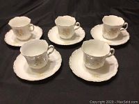 Five demitasse cups arranged with their matching saucers on a dark cloth background.