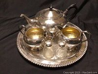 Front angle view of the entire silver plated tea set on the tray, including teapot, milk creamer, sugar bowl, and salt and pepper shakers.