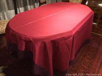 Tablecloth spread on table showing fuchsia silk fabric and purple hem border under warm lighting.