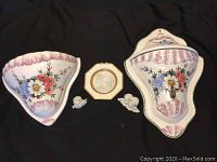 Two hand-painted Capodimonte wall vases, octagonal bisque porcelain plate and two small angel heads arranged on black cloth.