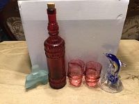 Lot contents showing cranberry bottle, two cranberry glasses, blue dolphin figurine, and frosted glass inukshuk sculpture against white background