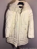 Front view of white quilted coat hanging on black hanger