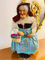Front view of antique Bernard Ravca doll with detailed face, lace collar, bonnet, floral skirt and holding basket of flowers