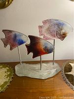 Front view of the three glass fish mounted on a single glass base showing the colors and metal rods.