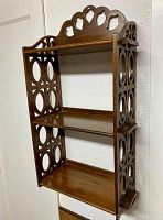 Front and side view of vintage wooden wall shelf with decorative cutouts and three shelves showing overall condition.