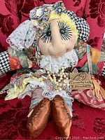 Full frontal image of Curiosity Lady fabric doll seated on a red velvet background showing clothing pattern, facial details, and accessories including the tag and pouch.