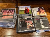 Photo of multiple music CD jewel cases piled on a hardwood floor including '20 Years of Beautiful Music', Charlotte Church albums, Mantovani Orchestra, and Joel Schwartz
