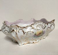 Side angled view of the antique porcelain dish showing detailed gold gilding and hand painted flower design.
