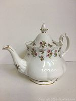 Side view of white bone china tea pot with rose and floral motifs, gold trimmed spout and handle, and high domed lid with finial.