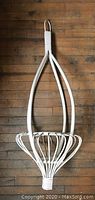 Full view of the white rattan plant pot holder hanging vertically on a wooden floor background, showing its curved design and loop top.
