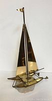 Full view of the brass sailboat sculpture showing smooth, polished sails and flag on mast.