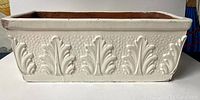 Full side view of the rectangular terra cotta planter showing white paint and raised leaf motifs.