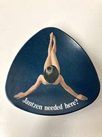 Front view of vintage triangular dish with blue background and top-down image of woman with legs crossed and arms extended, includes text 'Jantzen needed here?'.
