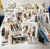 Photo showing a large pile of vintage women's sewing patterns from various brands, featuring illustrated models wearing dresses, tops, and pants.