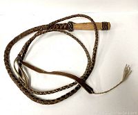 Full image of the coiled braided leather whip with wooden handle on white surface.