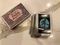 Vintage deck of cards with box showing Waddingtons English Playing Cards design and a stack of cards with black back featuring a man with a suitcase graphic in front of a globe.