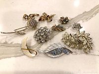 Overview of the 7 vintage brooches and 3 clip-on earrings arranged on white surface with marble pattern.