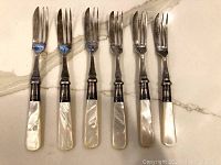 Six vintage forks with mother of pearl handles laid on marble surface showing full length and condition.