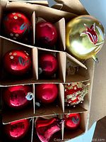 Box of vintage red glass ball Christmas ornaments with blue leaf paint and gold dots, along with one gold ornament with red floral design.