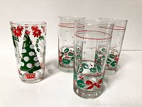 Four vintage drinking glasses with Christmas-themed designs, three with holly and ribbon patterns and one with Christmas trees and poinsettias.