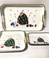 Three vintage Christmas trays of different sizes arranged on a white surface, showing the Christmas tree design with ornaments, presents, and stars on a white background.