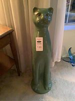 Full front view of tall green ceramic cat on carpet in front of curtain, showing its height relative to furniture.