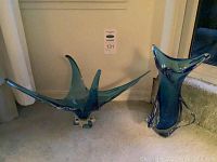Two teal-blue glass vases side by side against wall