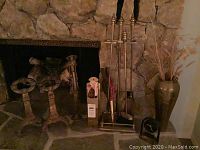 Wide shot showing brass fireplace accessories including andirons, tool set, and floor vase in front of stone fireplace.