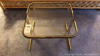 Overview of brass frame side table with glass top on carpeted floor.