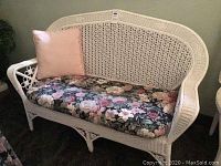 Front view of white wicker settee with floral cushion and pink throw pillow.
