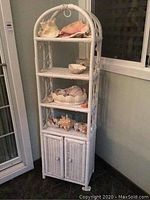 Full view of the white wicker shelf with seashells displayed on shelves and cabinet at bottom
