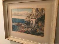 Framed painting showing an Italian coastal scene with cliffs, buildings, and sea in the background.