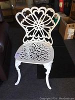 Full view of the white iron chair showing ornate backrest, seat, and curved legs.