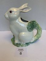 Side view of the white ceramic bunny pitcher showing detailed face, ears, and green leafy handle shaped like a vine curling at the base.
