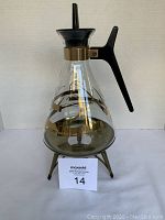 Front side of the vintage Inland Glass coffee pot on metal stand showing gold swirl pattern and black handle