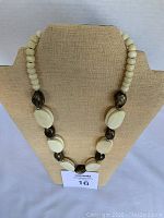 Full view of the bead necklace displayed on a beige stand showing cream double beads alternating with bronze colored beads.