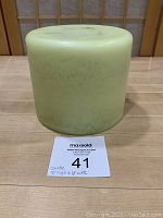 Front view of large pale green candle, showing smooth cylindrical shape and size relative to label.