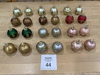 All 24 holiday place card holders shown in rows grouped by color, featuring gold, brown, red, green, white, pink, and silver ornaments with flattened bottoms and hanging loops on top.