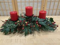 Frontal view of the holiday centre piece showing the artificial greenery with red berries and the three red pillar candles.