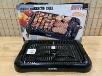Sanyo indoor electric barbecue grill in front of original box with food image graphics.
