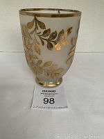 Front and side view of a frosted glass vase with gold-colored leaf pattern and gold rim. Shows overall vase shape and decoration details.