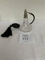 Photo of clear glass perfume atomizer with etched flower pattern, silver-tone top, black bulb atomizer with tassel on a white surface, measured at 5.5 inches high
