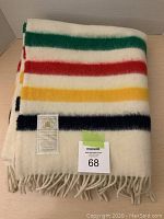 Folded throw showing signature green, red, yellow and navy stripes and fringe with lot tag visible