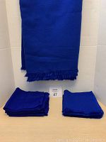 Dark blue folded tablecloth hanging with stacks of matching napkins below, showing fabric texture and fringed edges.