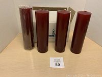 Four burgundy pillar candles displayed standing upright next to a MaxSold auction number card and white box.