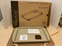 Pampered Chef medium bar pan in front of its original box, includes mini scraper and booklet shown on top of the pan.