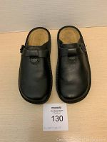 Top-down view of the pair of black leather slip-on clogs showing the rounded toe and buckle strap details.