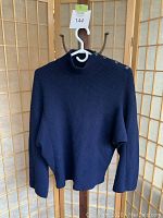 Front view of navy blue ribbed sweater showing shoulder button detail, wide sleeves, fitted hem